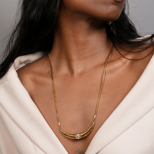 Gold necklace with a diamond pendant worn by a person against a neutral background