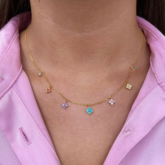 Gold necklace with colorful pendants worn by a person in a pink shirt.